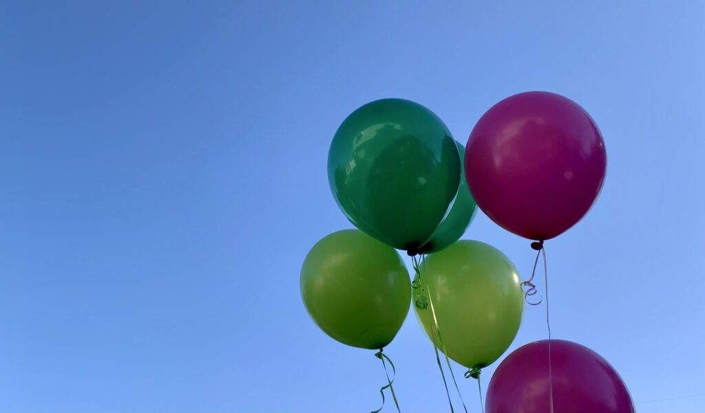 pink and green helium balloons blue sky